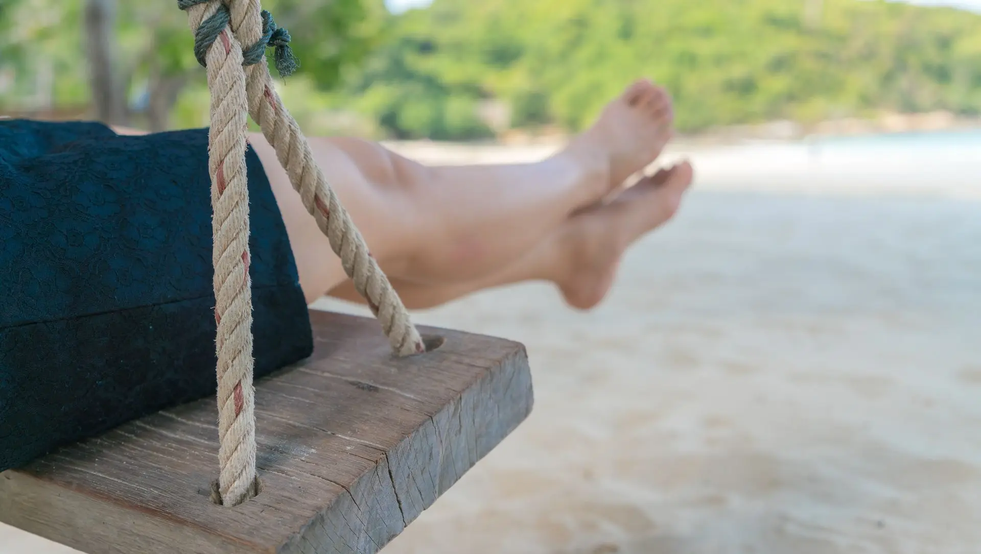Hombre sentado en columpi en la playa con pies cruzados