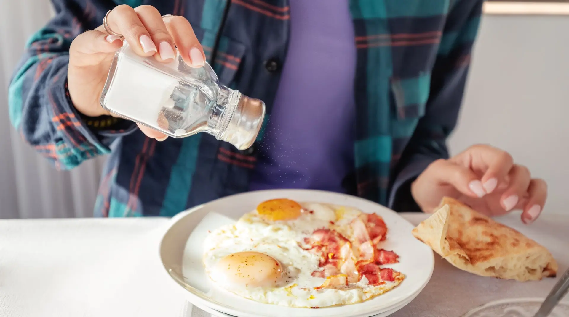 Persona sentada colocando sal con un salero a un plato con huevos fritos y una tortilla